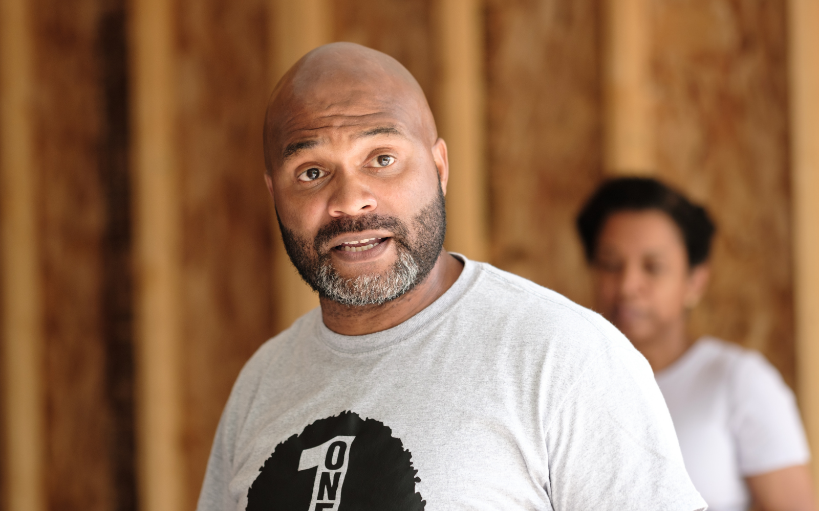 A Black man with beard and light gray t-shirt speaking to audience off camera