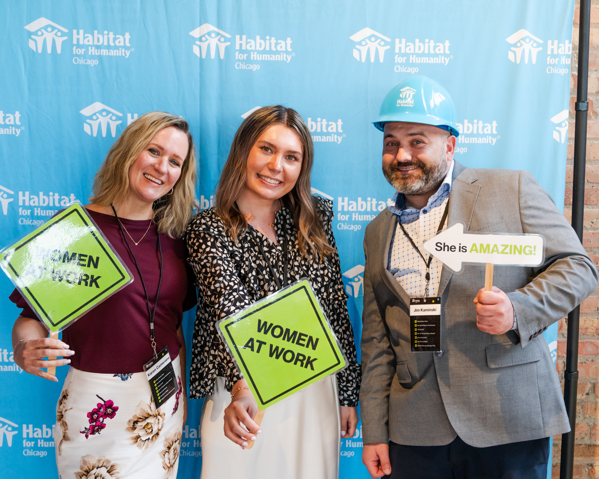 Three people holding props and smiling in front of branded backdrop