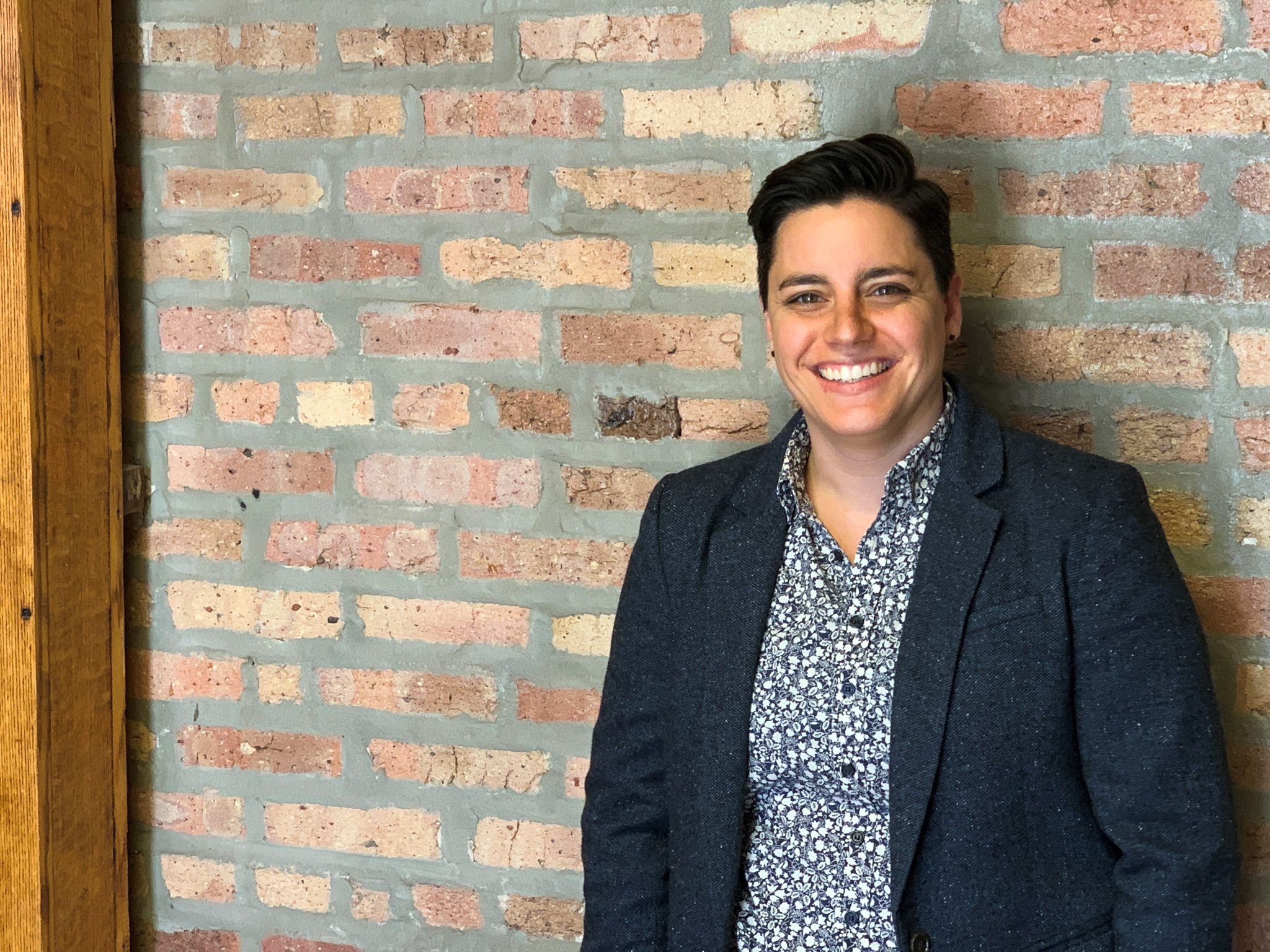 Short-haired woman smiling in front of brick wall