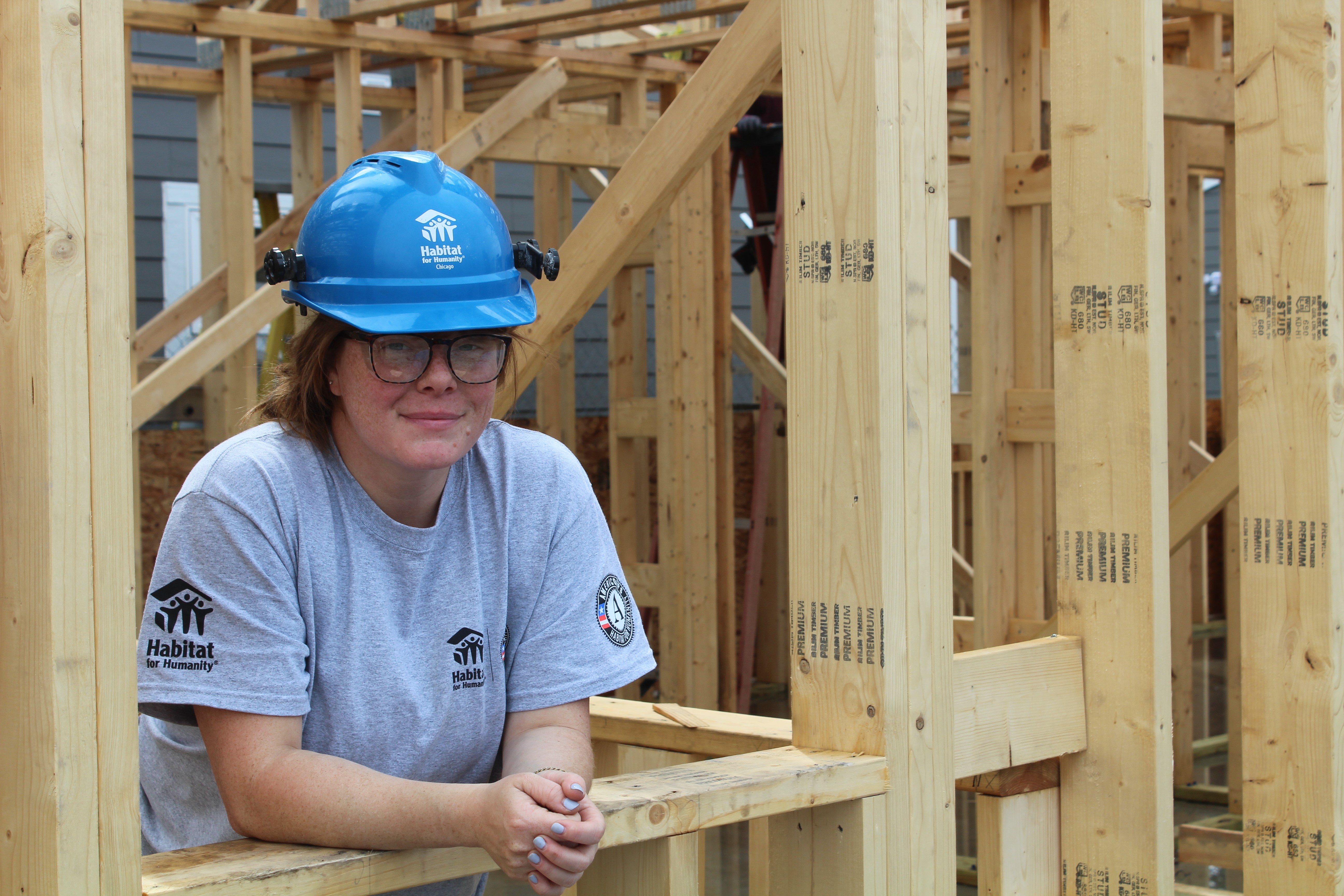 Woman on construction site, wearing helmet and leaning on framing