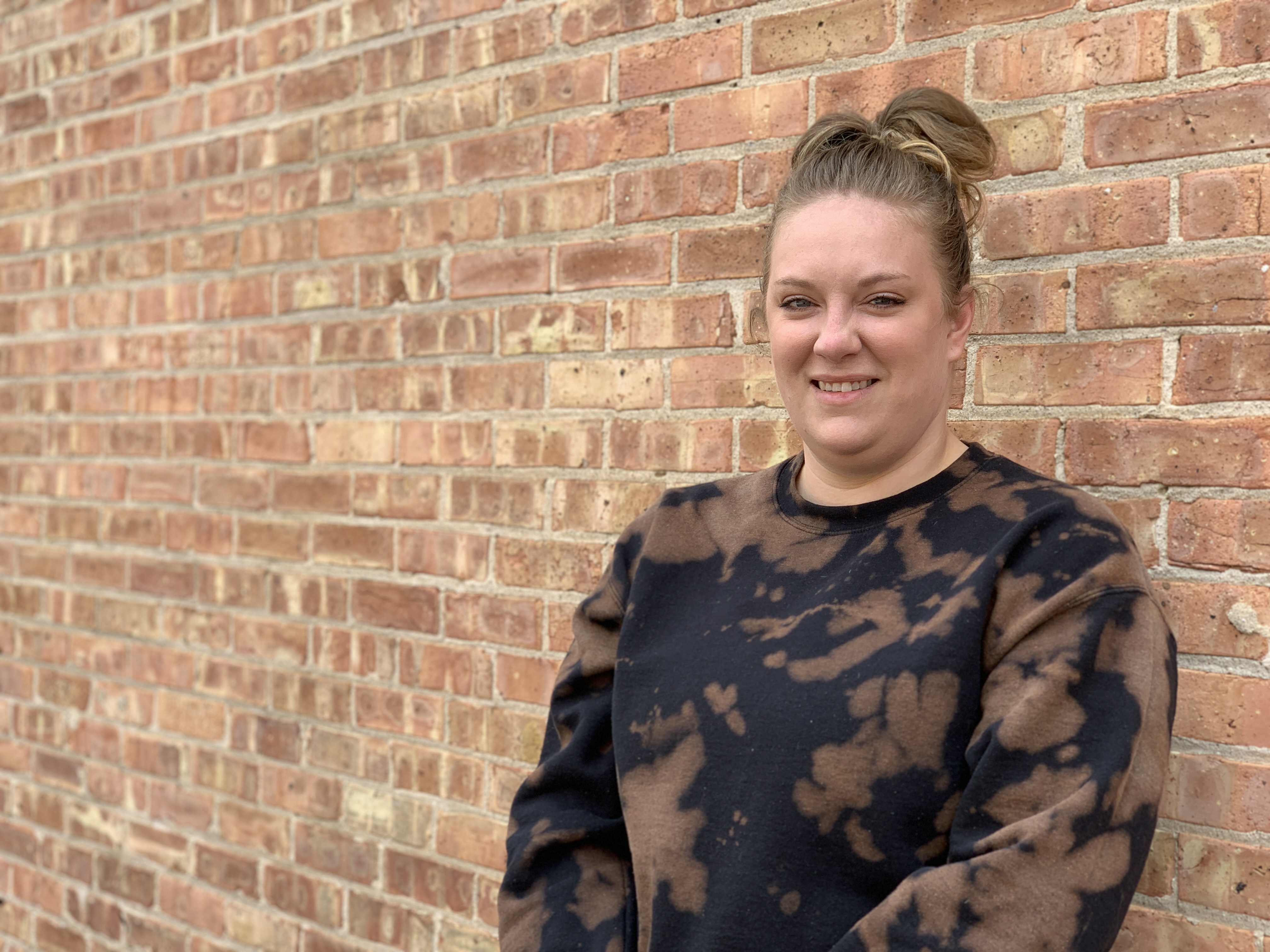 Woman smiling at camera in front of brick wall