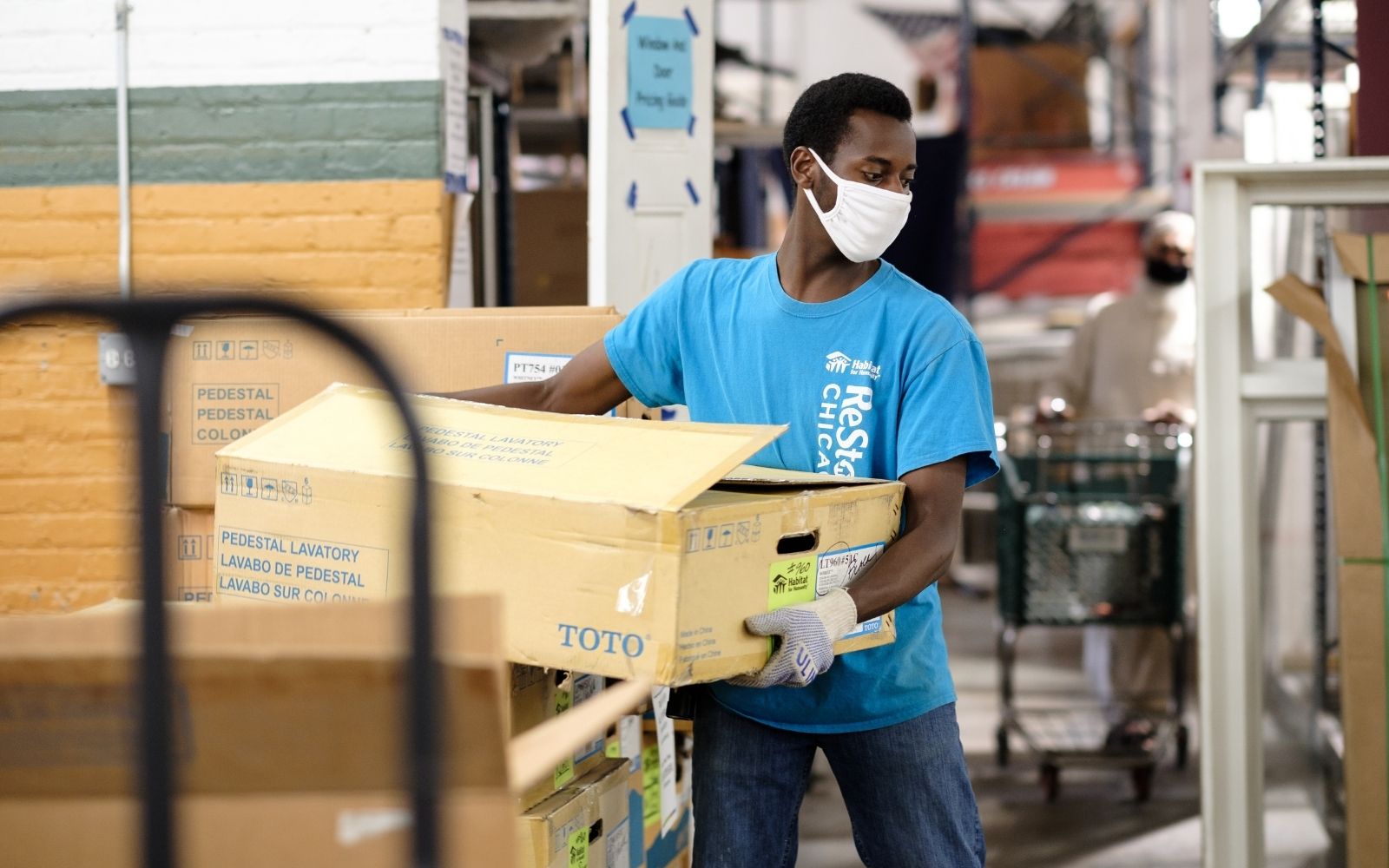 Man wearing blue shirt moving boxes and wearing a face mask