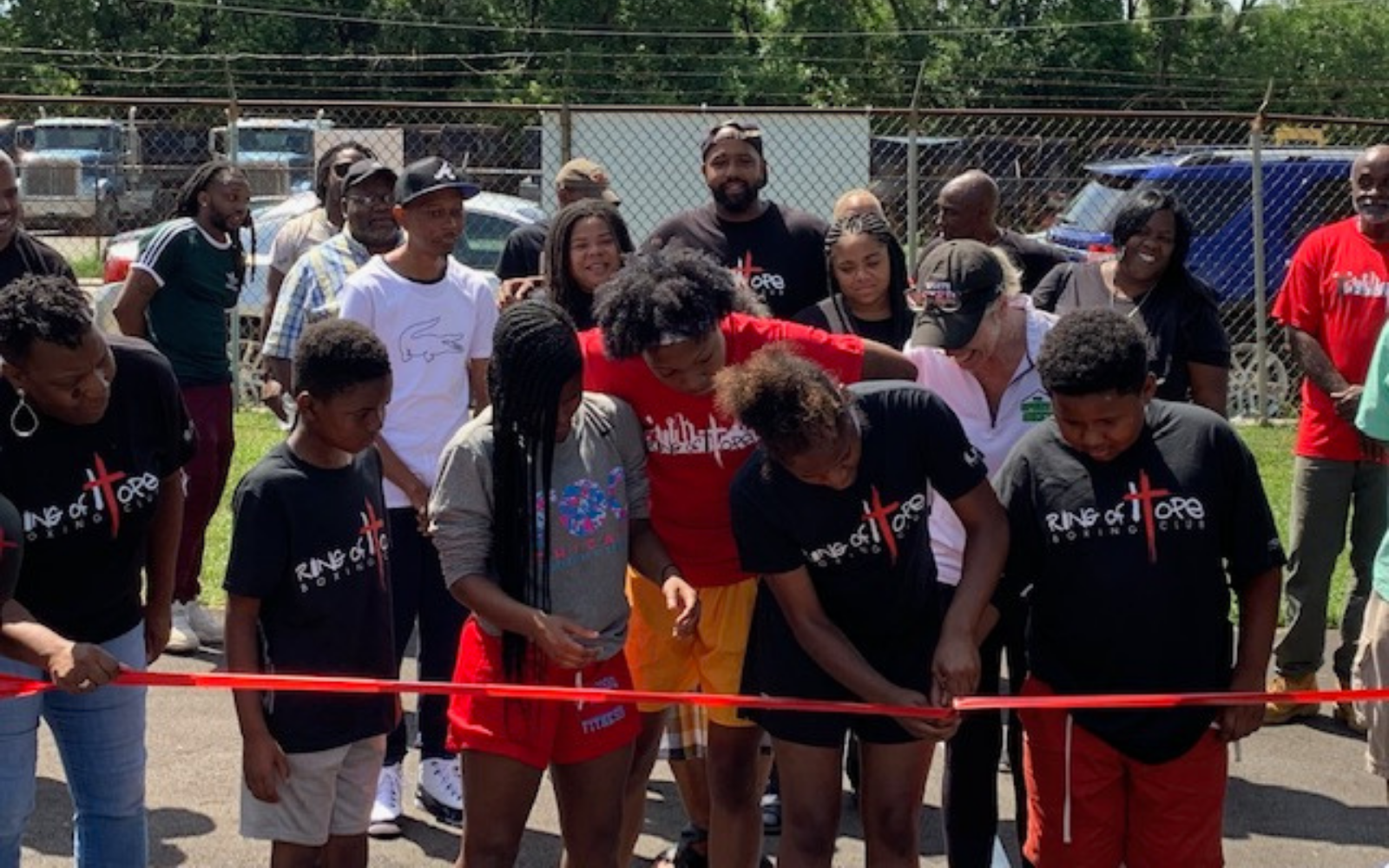 Group of Black children cutting a red ribbon with community members behind