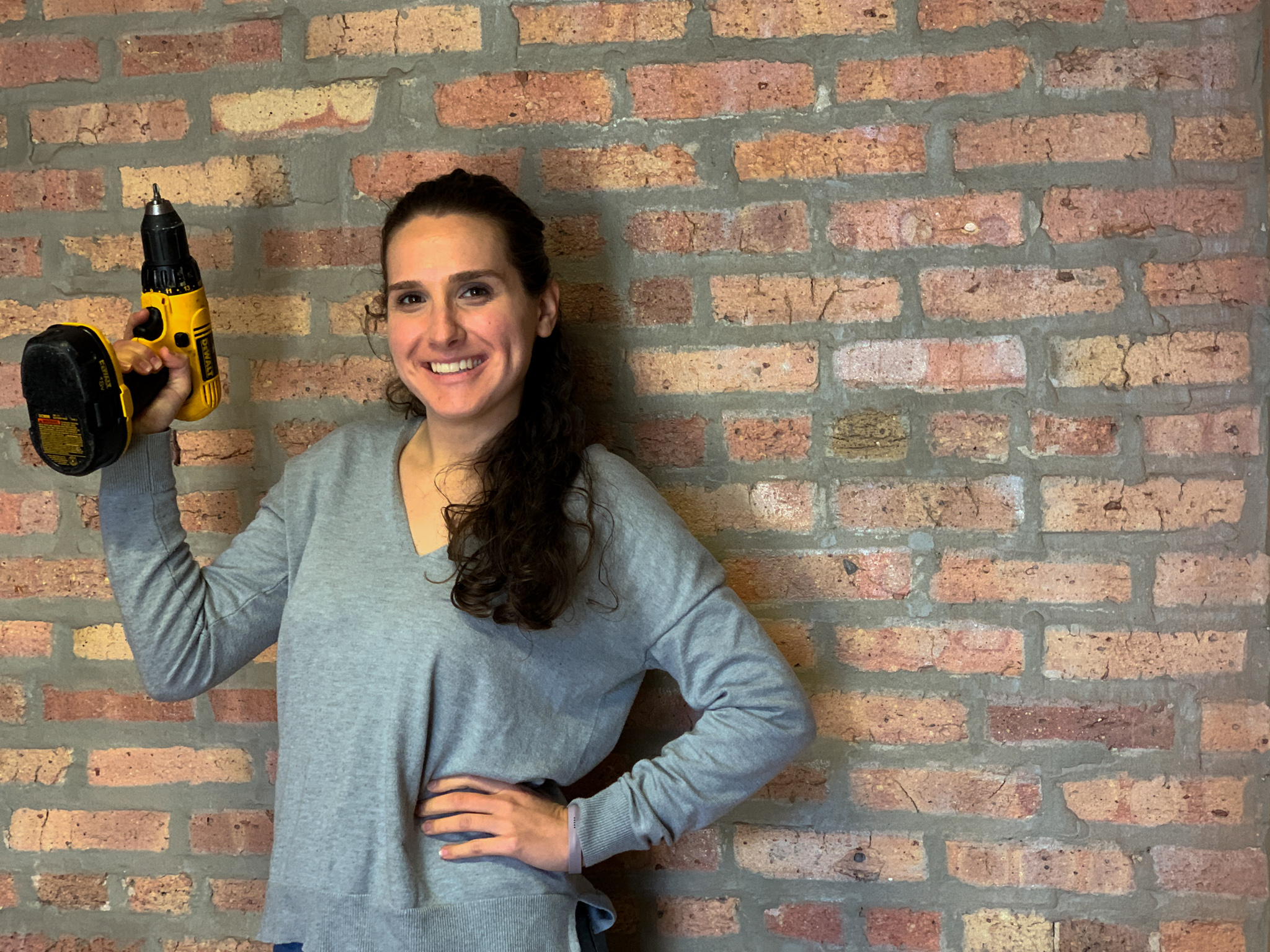 Woman holding up a power drill in front of brick wall