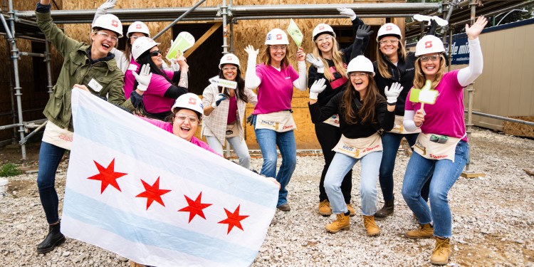 Group of people on a build site with hard hats, matching shirts, and fun props