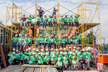 The 2017 Women Build volunteers flank the scaffolding of the home they funded and are helping build