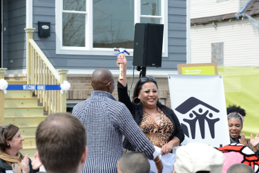 Homebuyer Holding Up Hammer During Ceremony with Others Clapping Around