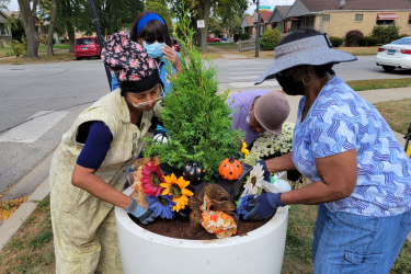 Four women planting small tree with festive decor in large planter