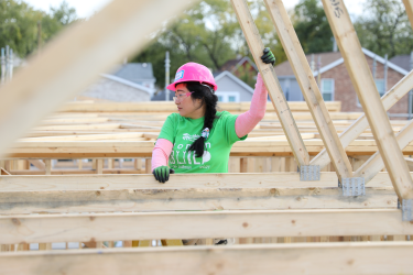 Asian Women Build volunteer gazing off screen while holding roof trusses steady