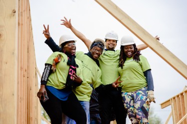 A group of volunteers and homebuyers pose for a photo on the build site