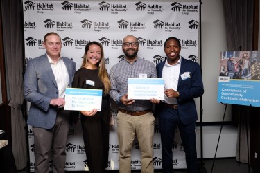 Four young professionals holding signs and standing in front of branded backdrop