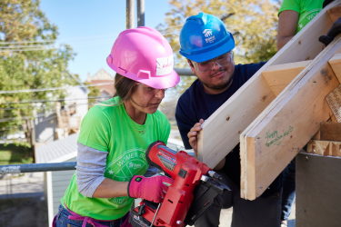 Construction crew leader helping a volunteer with a nail gun