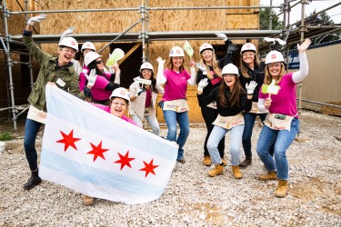 Group of people on a build site with hard hats, matching shirts, and fun props