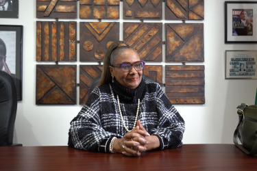 Woman wearing black and white sweater smiling, sitting at a desk