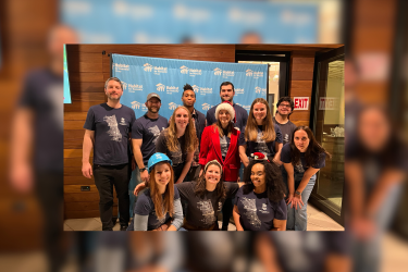 Group of people wearing matching shirts, smiling in front of a branded backdrop