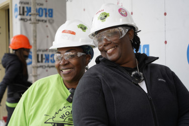 Two women wearing hard hat and safety glasses on build site, smiling