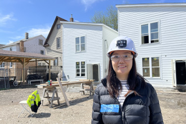 Woman in hard hat and safety glasses on a build site with houses behind them