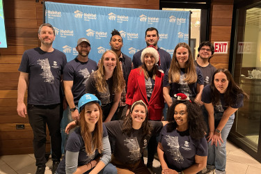 Group of people wearing matching shirts, smiling in front of a branded backdrop